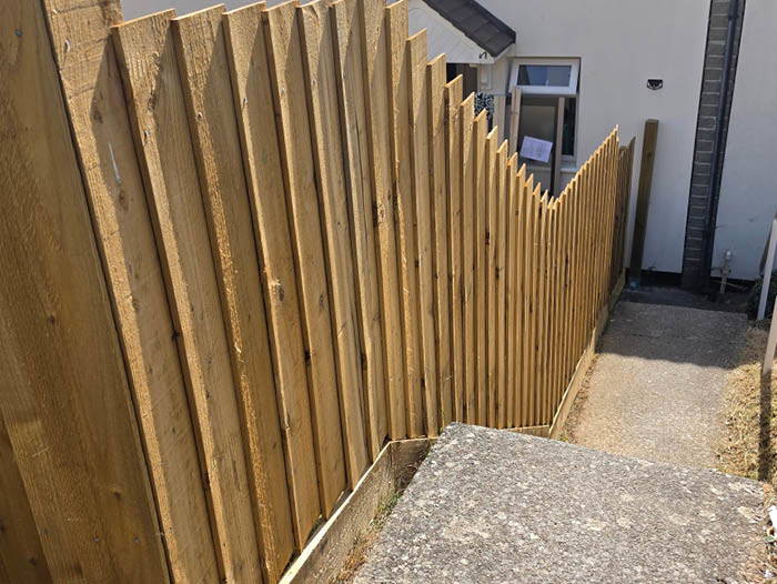 Fence repairs and maintenance in Plymouth showing new timber panels installed along a sloped pathway.