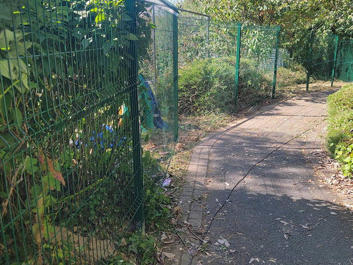 Metal commercial fencing installation in Plymouth alongside a paved walkway with surrounding vegetation.