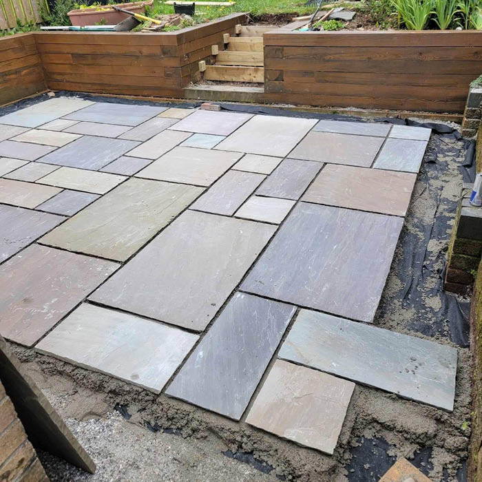 Patio layers in Plymouth installing a new stone slab patio with timber retaining wall during work in progress. Patio layers in Plymouth installing a new stone slab patio with timber retaining wall during work in progress.